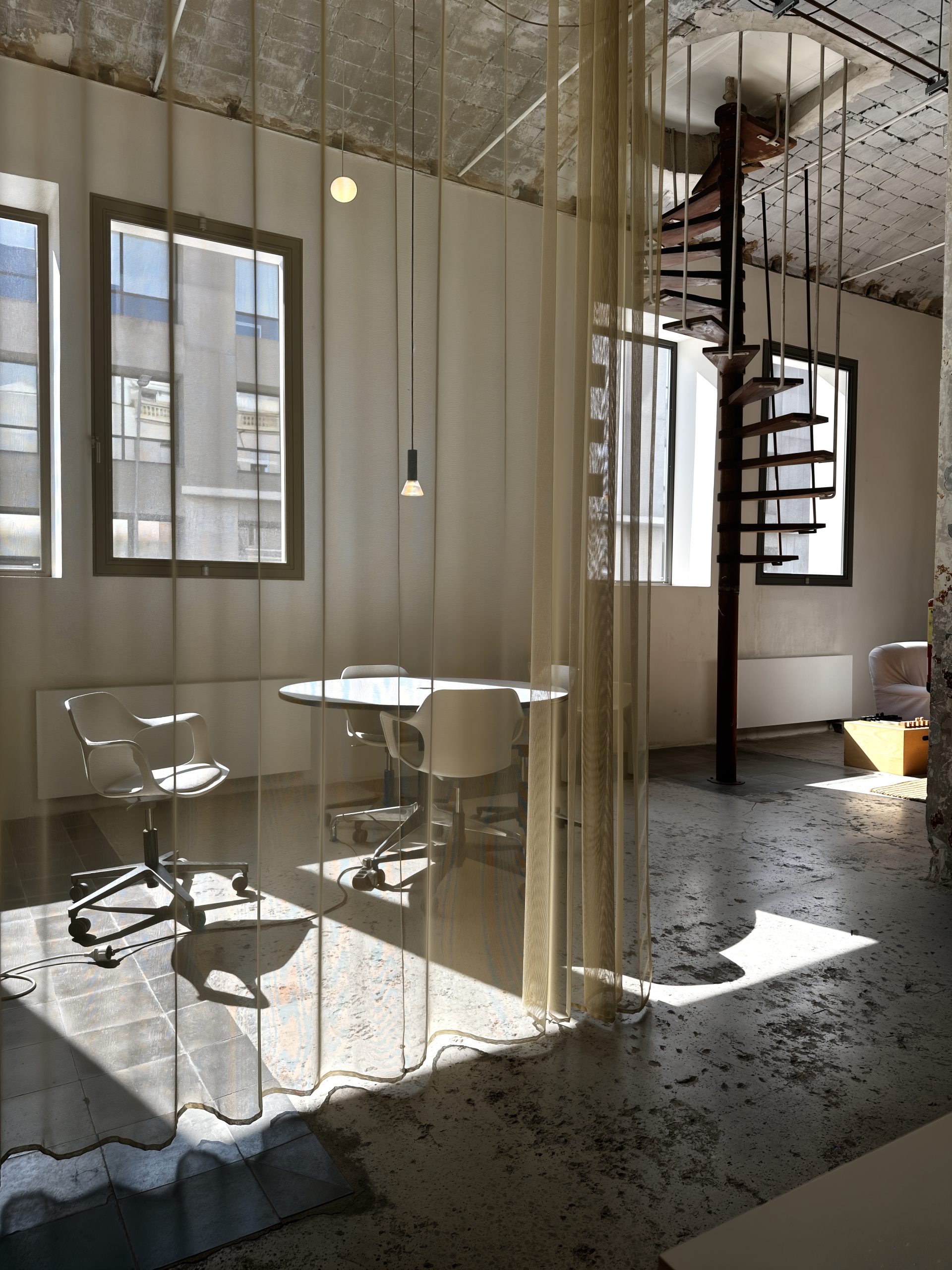 Sunlit interior at Montoya with sheer curtains, a round table, and a spiral staircase.